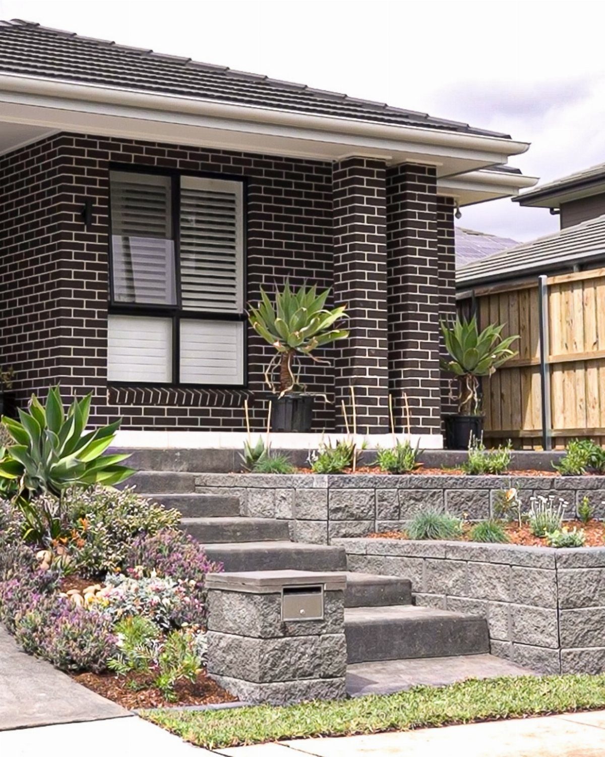 26 Front Garden Ideas for Curb Appeal and Small Yards 3 Modern front garden with tiered stone walls and a variety of succulent plants.