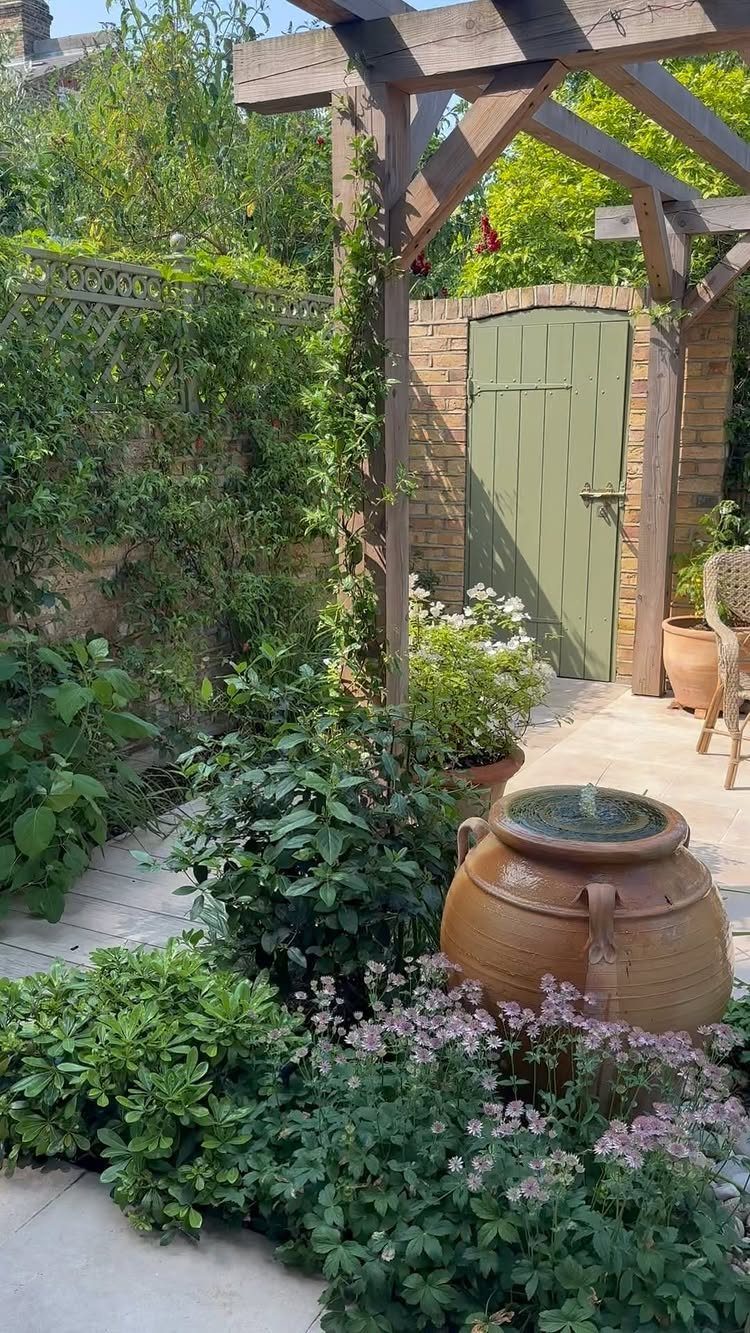 26 Front Garden Ideas for Curb Appeal and Small Yards 20 Garden with a wooden pergola, green door, and terracotta water jar among flowers.