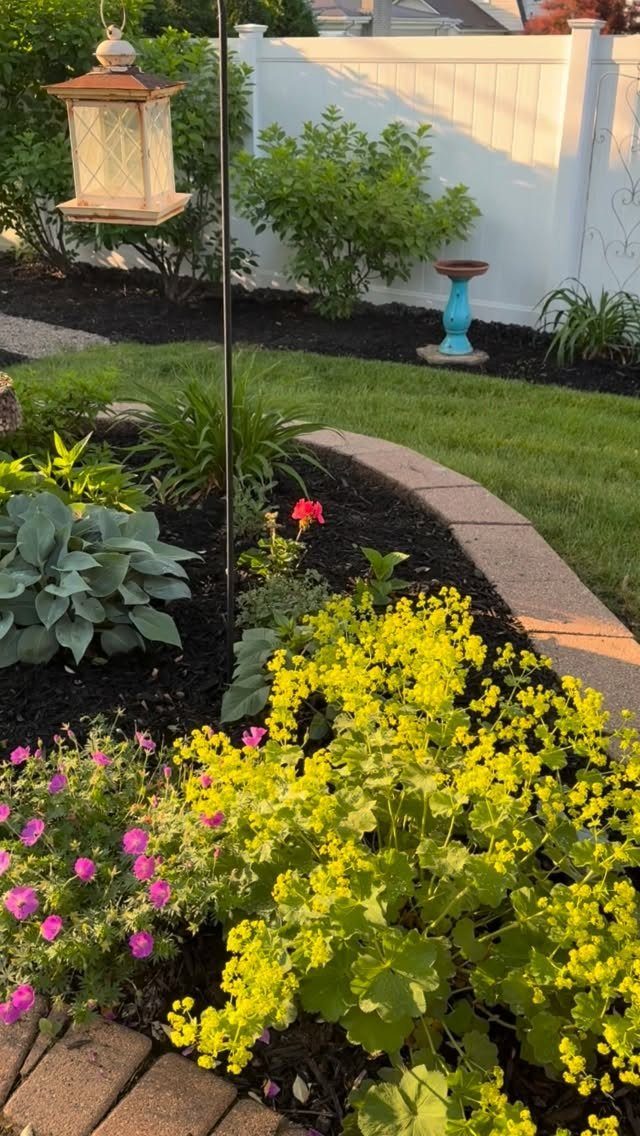 Curved garden bed with yellow and pink flowers and a stone border.