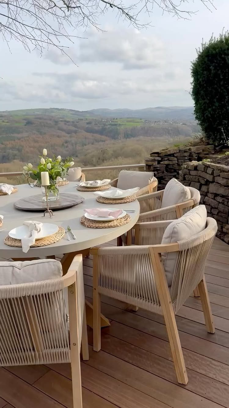 Round dining table and woven chairs on a wooden deck overlooking rolling hills.