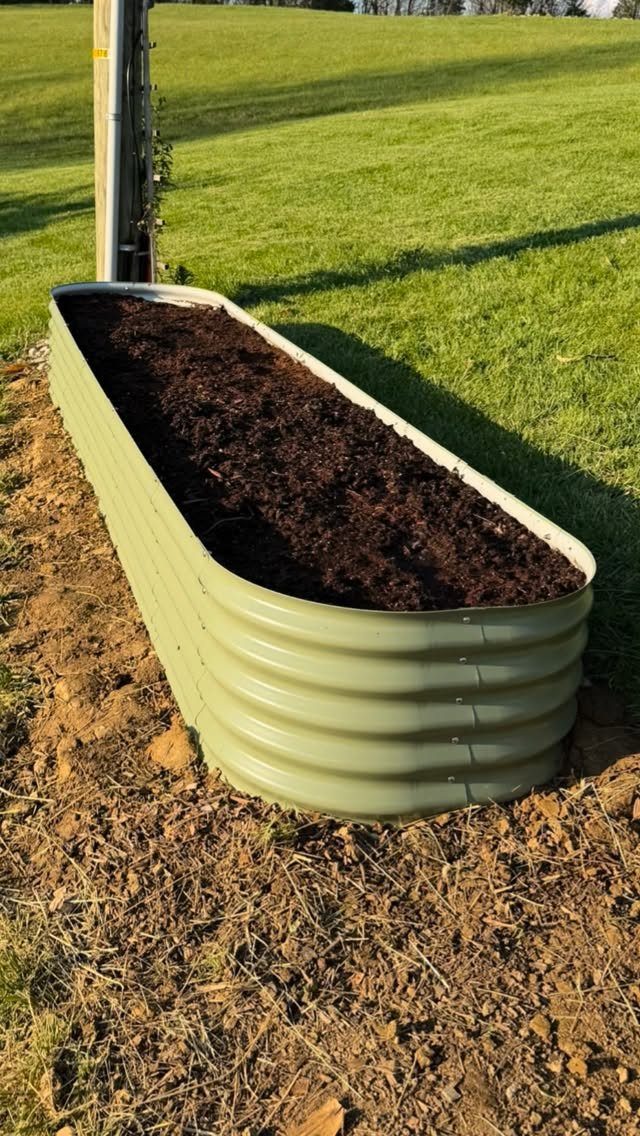 Corrugated metal raised garden bed filled with dark soil on a green lawn.