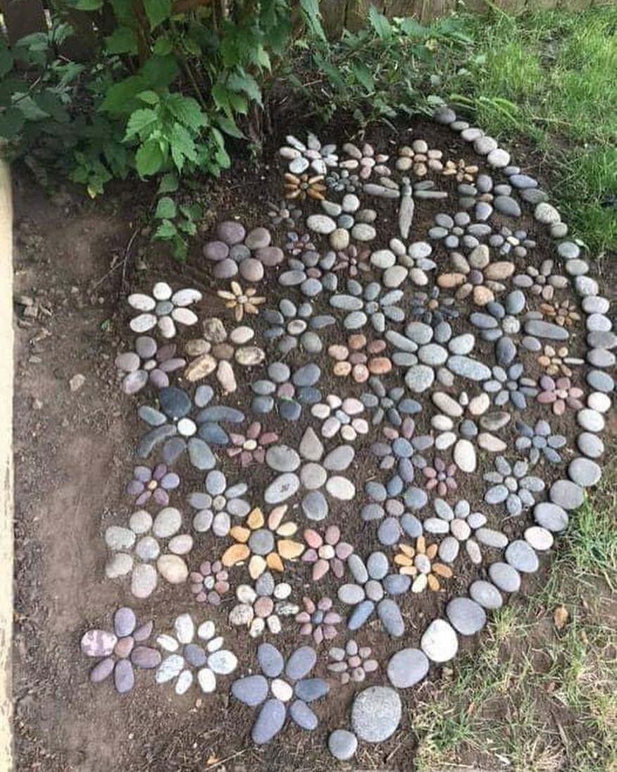 Pebble mosaic of flowers and a dragonfly arranged in a garden bed