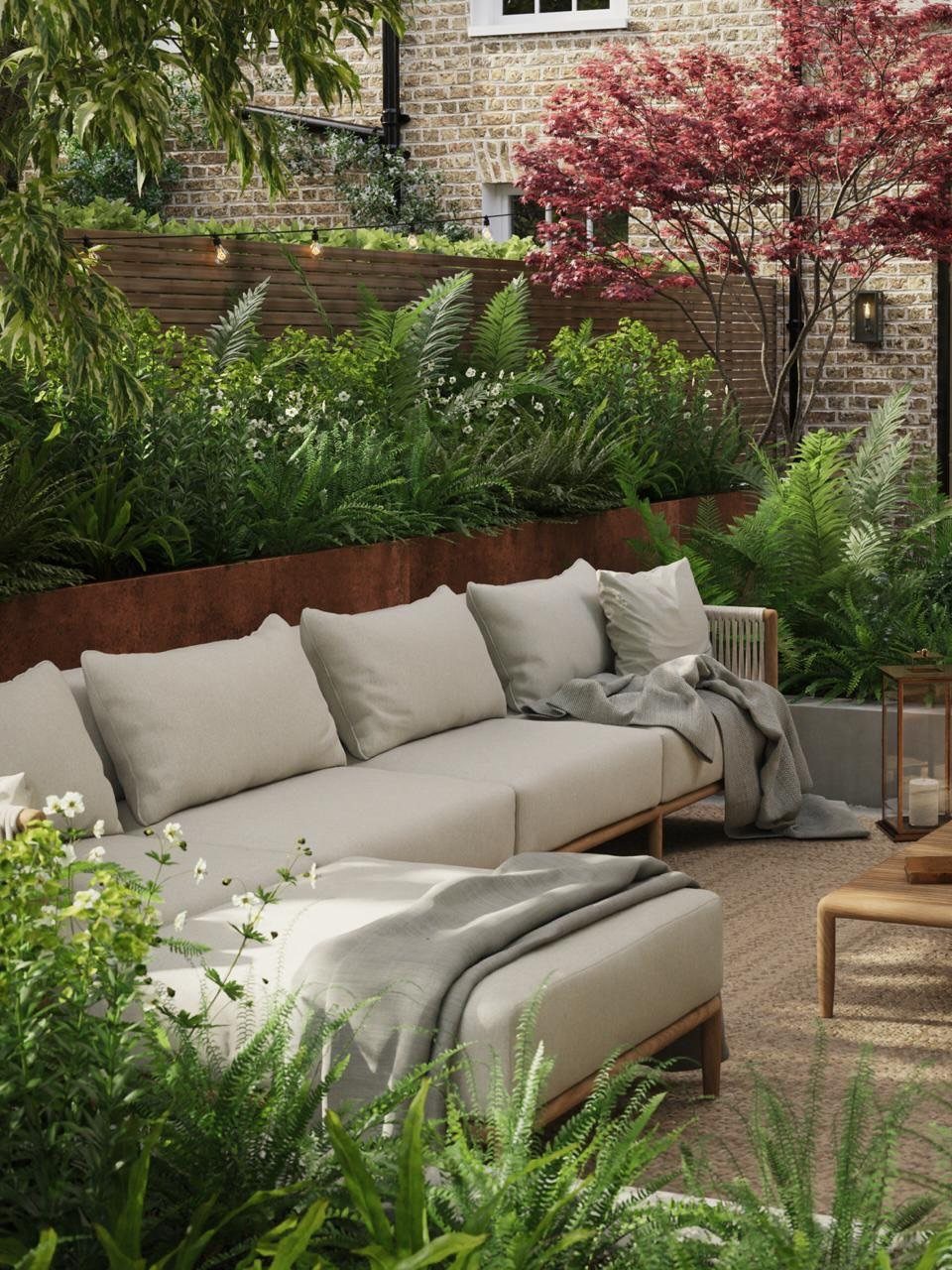 Modern outdoor lounge with grey sofa and lush green ferns in rusted planters.