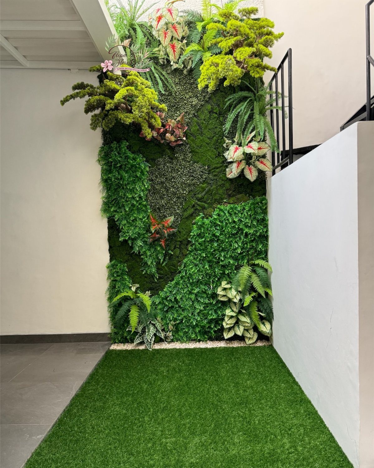 Vertical garden wall with diverse green plants and ferns above artificial grass flooring.