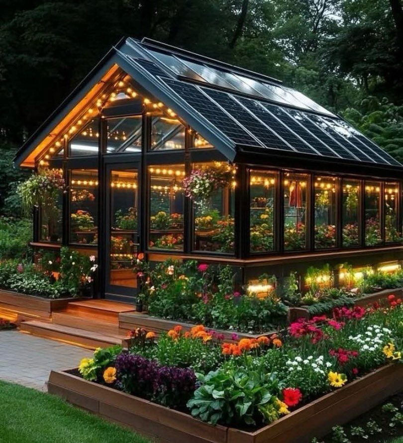 Modern glass greenhouse with solar panels on the roof and colorful flower beds.