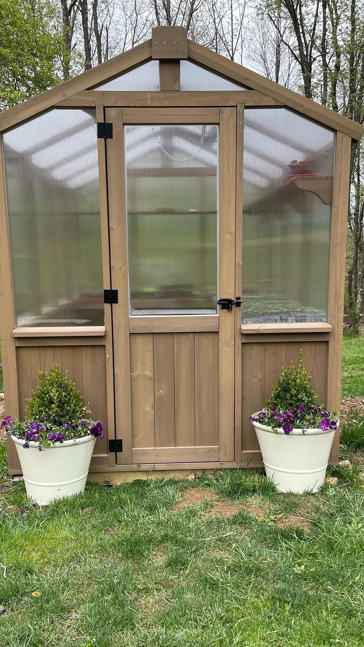 Wooden greenhouse with translucent walls and white flower pots on a grassy lawn