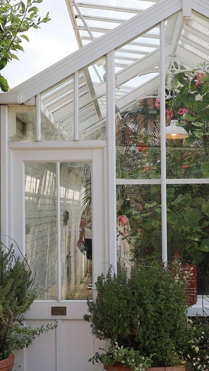 Green House Layout: 17 Ideas for Benches, Beds and Lighting 5 White glass lean-to greenhouse attached to a building with lush green plants inside.