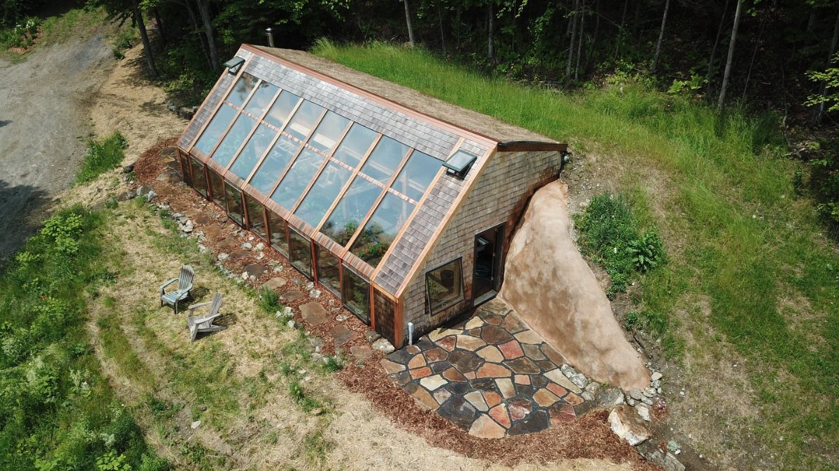 Greenhouse with slanted glass roof and shingled walls built into a grassy hillside