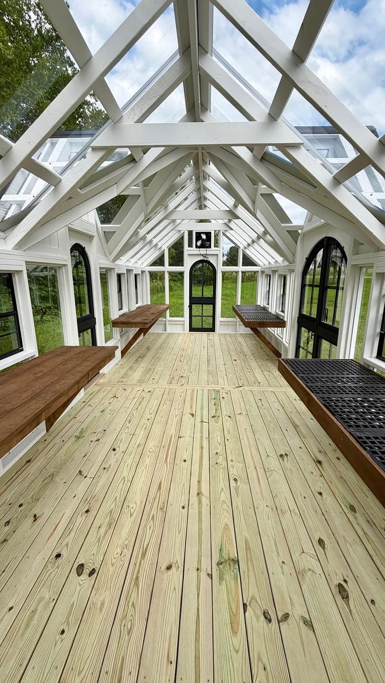 White wooden greenhouse interior with clear roof panels, wooden flooring, and potting benches.