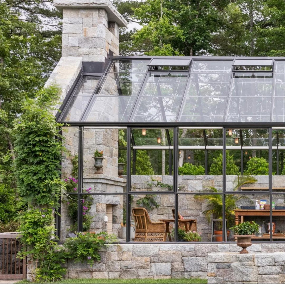 Glass greenhouse with black frames built on a low grey stone plinth foundation.