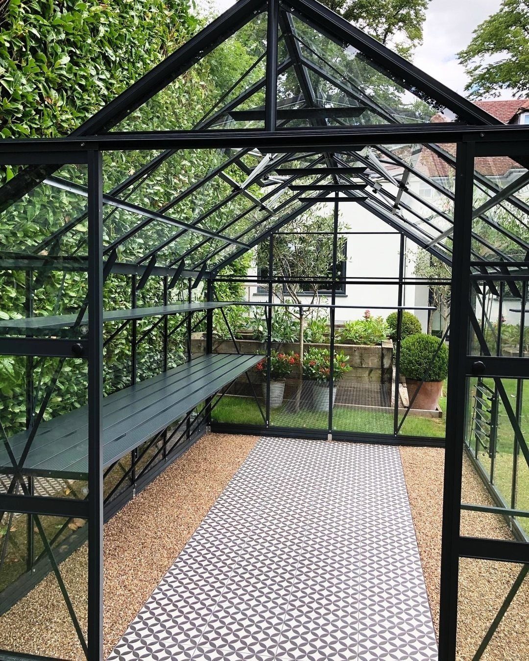 Patterned runner rug and gravel flooring inside a black glass greenhouse.