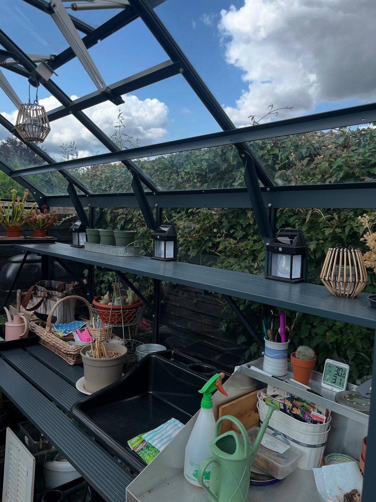 Greenhouse interior with organized shelves, gardening tools, and a potting station sink.