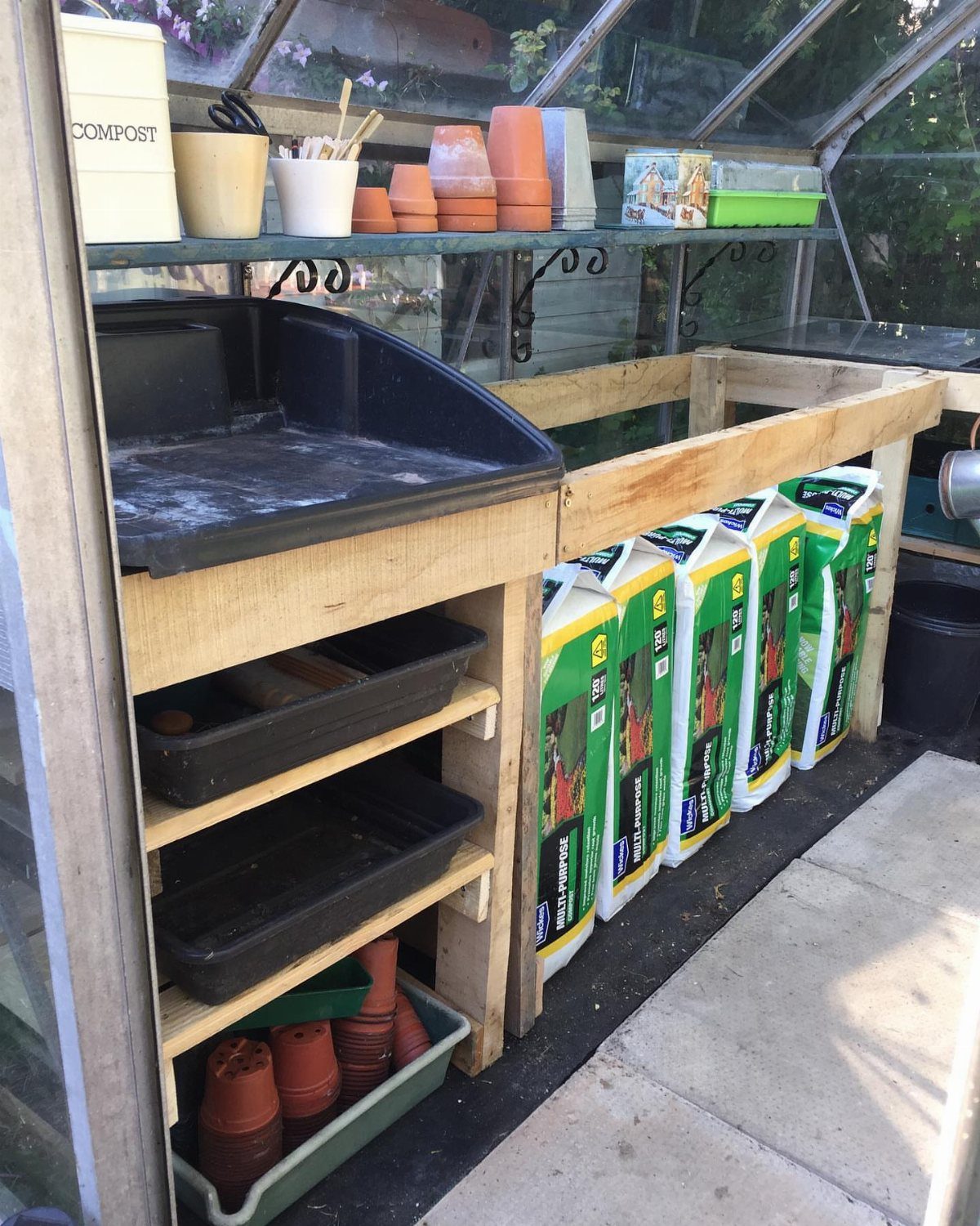 Wooden shelving unit in a greenhouse holding soil bags and potting trays