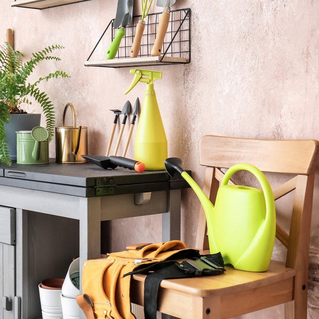 Black wire wall rack holding gardening hand tools above a grey potting workbench.