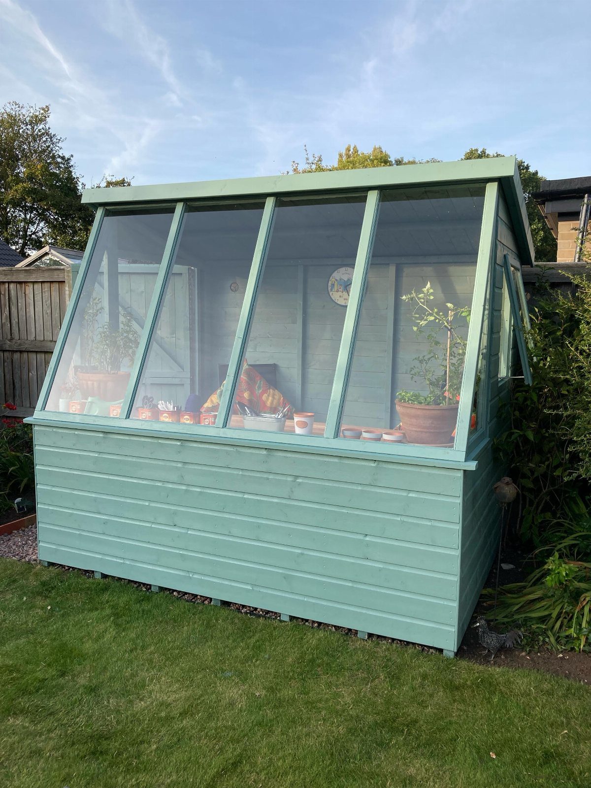 Light green farmhouse garden shed with glass greenhouse panels on a grassy lawn