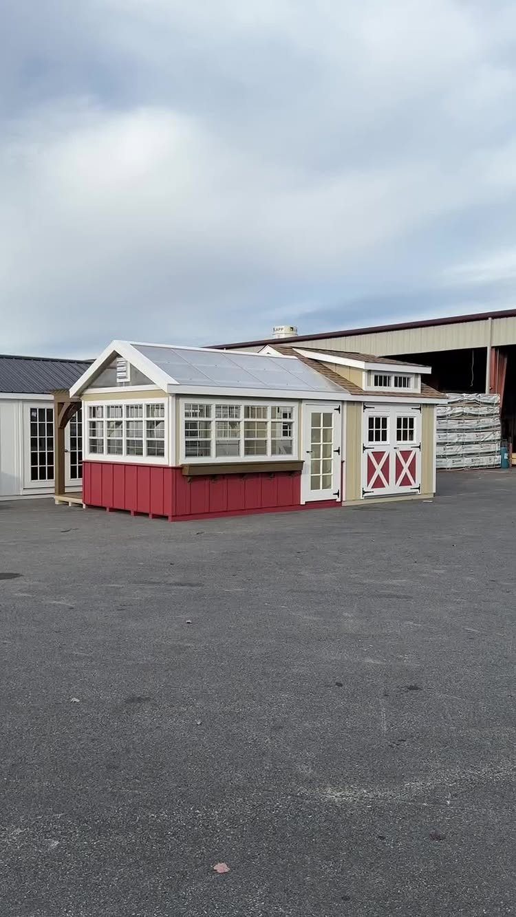 Combined greenhouse and storage shed with red and white siding on asphalt lot