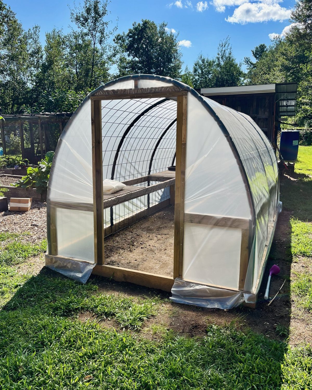 PVC hoop greenhouse with white plastic covering and a wooden frame entrance.