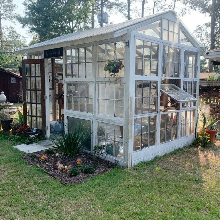 White wooden greenhouse made from salvaged window panes on a green lawn.