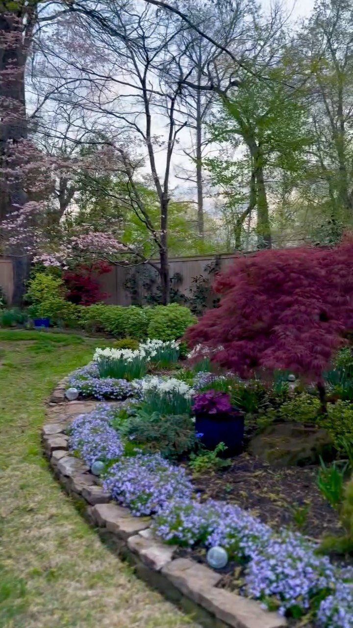 10 Ideas for Landscaping Around Trees, From Moss to Lighting 2 Curved stone garden bed with purple phlox, white flowers, and flowering cherry trees.