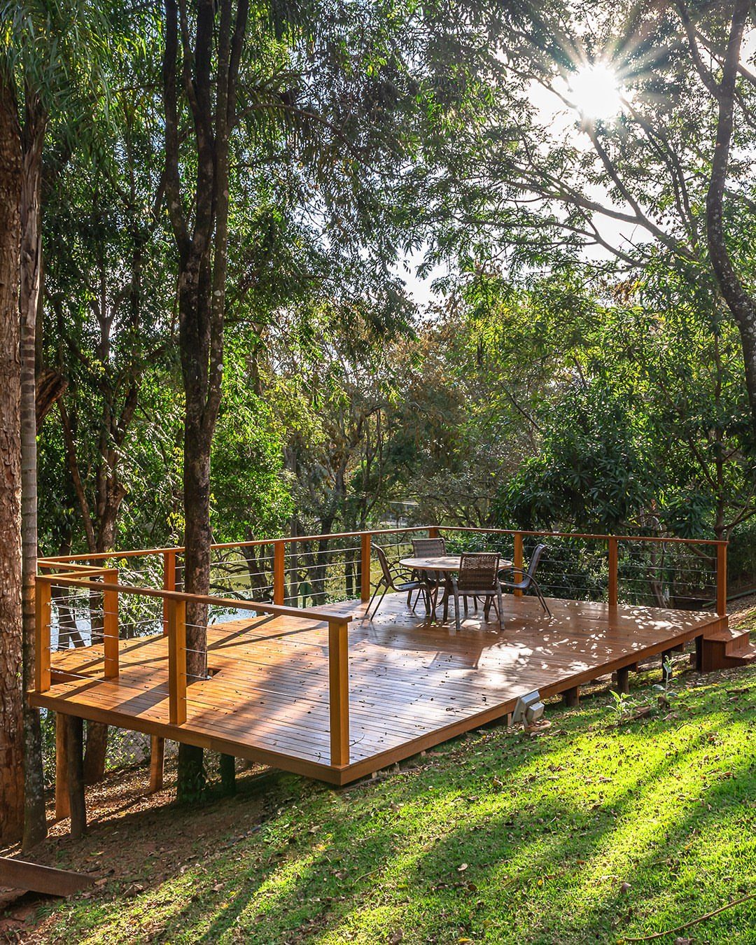 10 Ideas for Landscaping Around Trees, From Moss to Lighting 5 Wooden deck with dining furniture built around tall trees in a sunny forest.