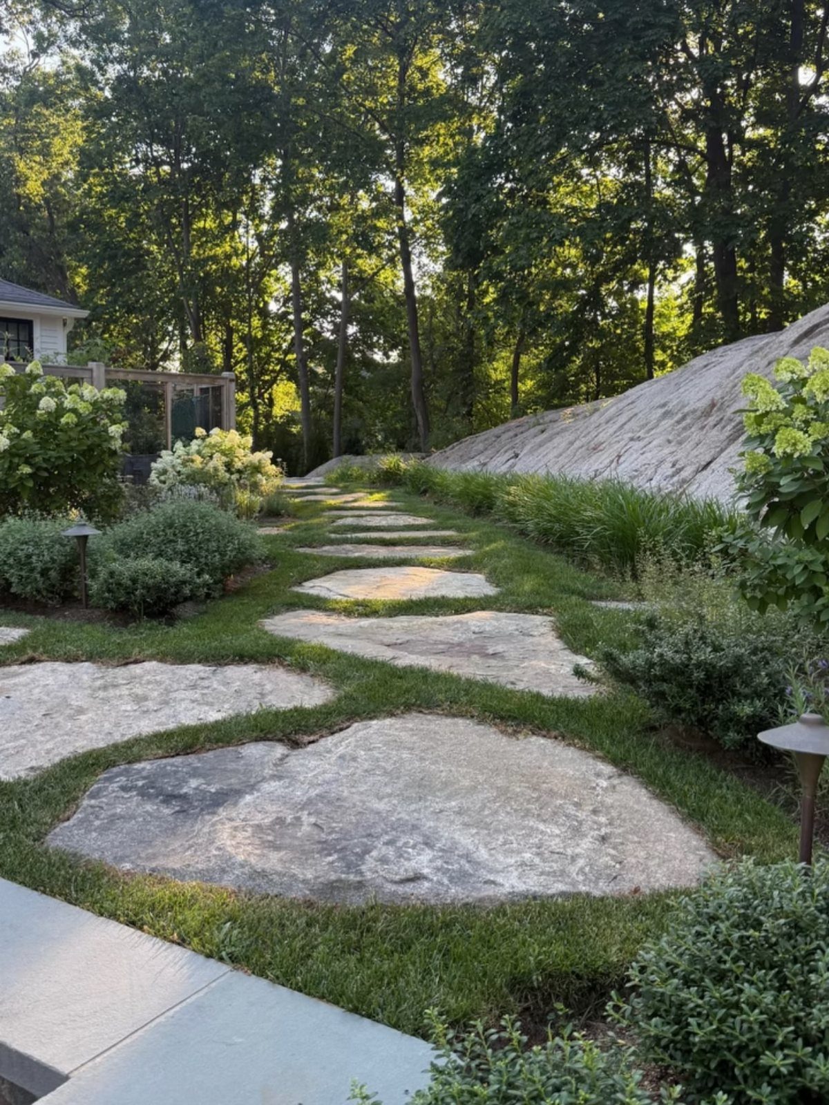 10 Ideas for Landscaping Around Trees, From Moss to Lighting 7 Stone stepping path winding through a green garden with shrubs and tall trees.