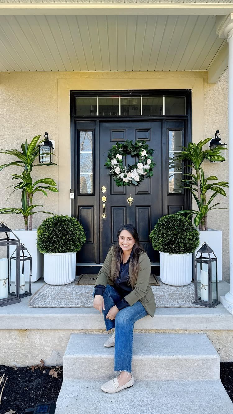 Large white ribbed planters with green foliage flanking a black front porch door.