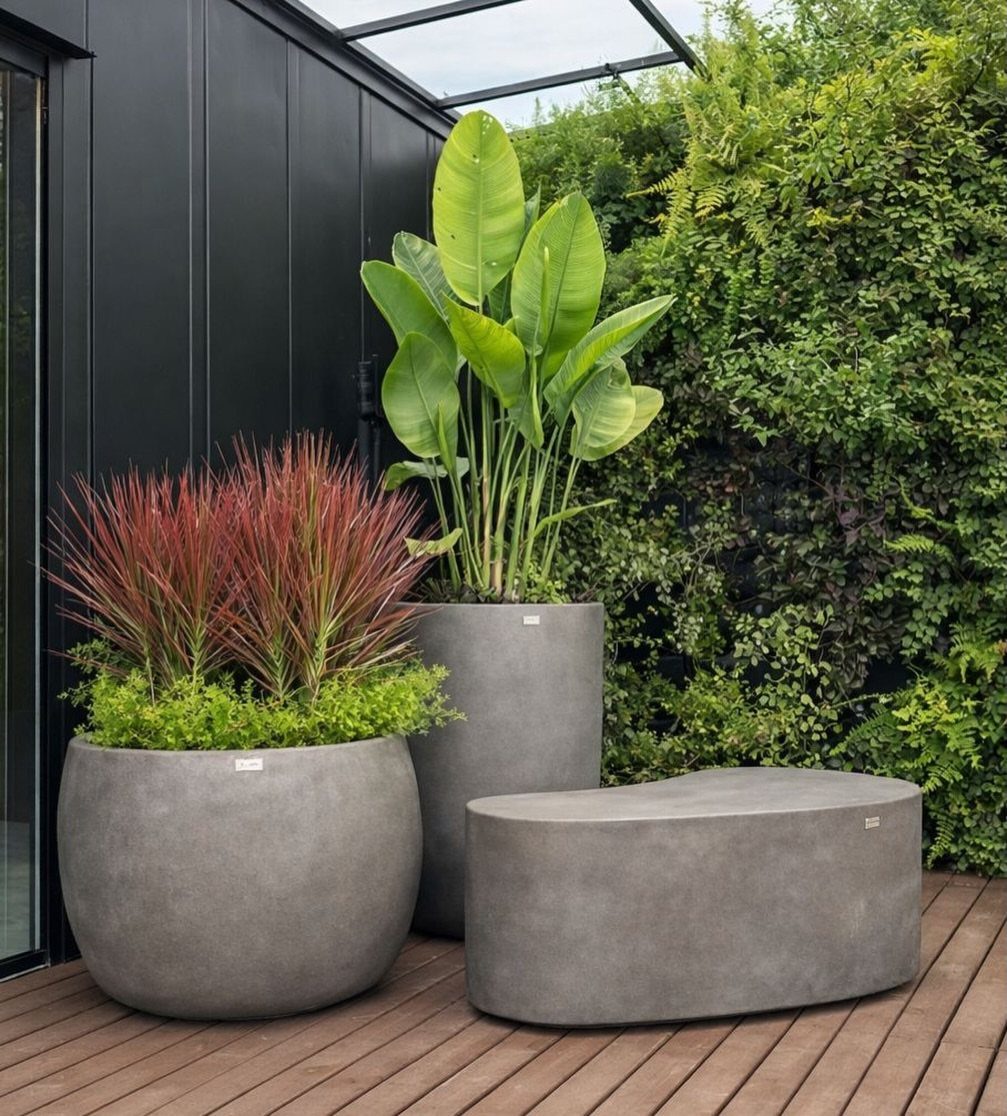 Large round grey concrete planters with foliage and a matching bench on a deck.