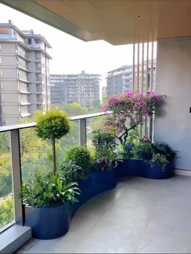 Curved navy blue planter with diverse greenery and pink flowers on a balcony.
