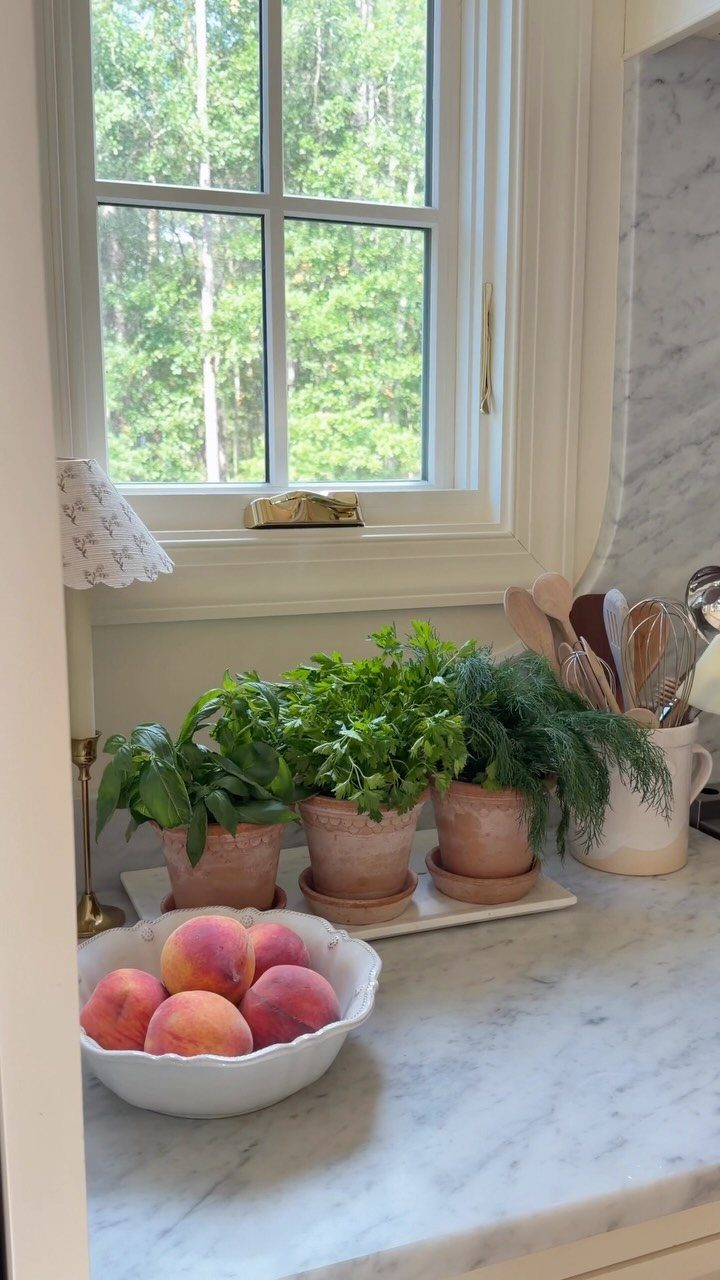 Three terracotta pots of fresh herbs on a white marble kitchen countertop.