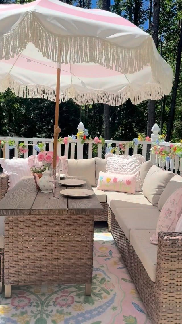 Wicker dining table and L-shaped sectional sofa under a pink fringed umbrella.
