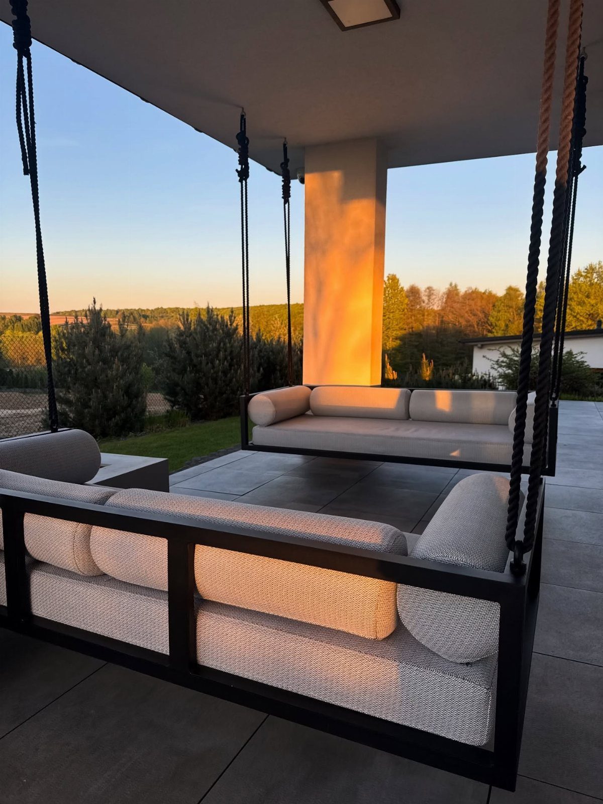 Two large black-framed daybed swings with grey cushions on a covered outdoor patio.