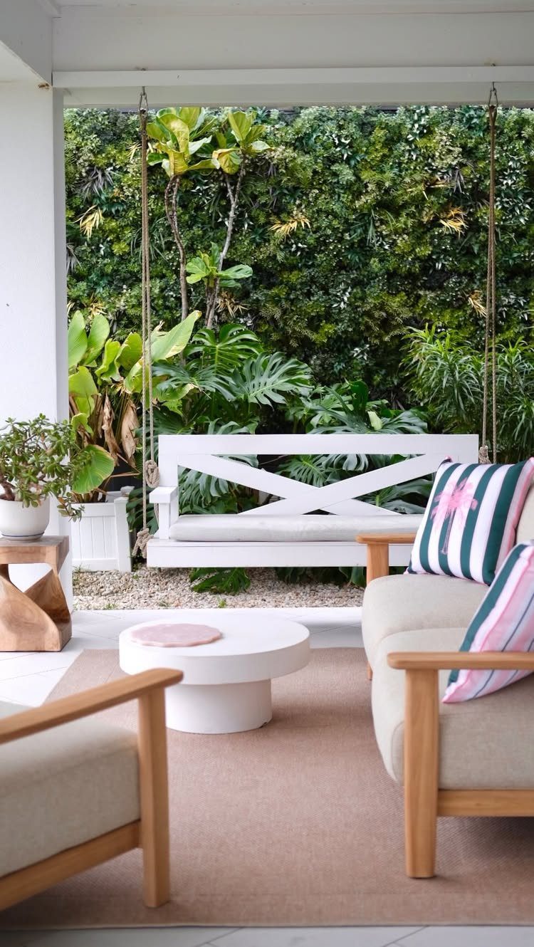 Modern patio with white coffee table, wooden armchairs, and a hanging daybed swing.