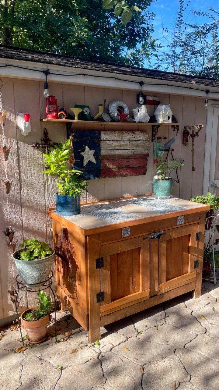 Wooden outdoor serving station with a countertop and shelving against a tan wall.
