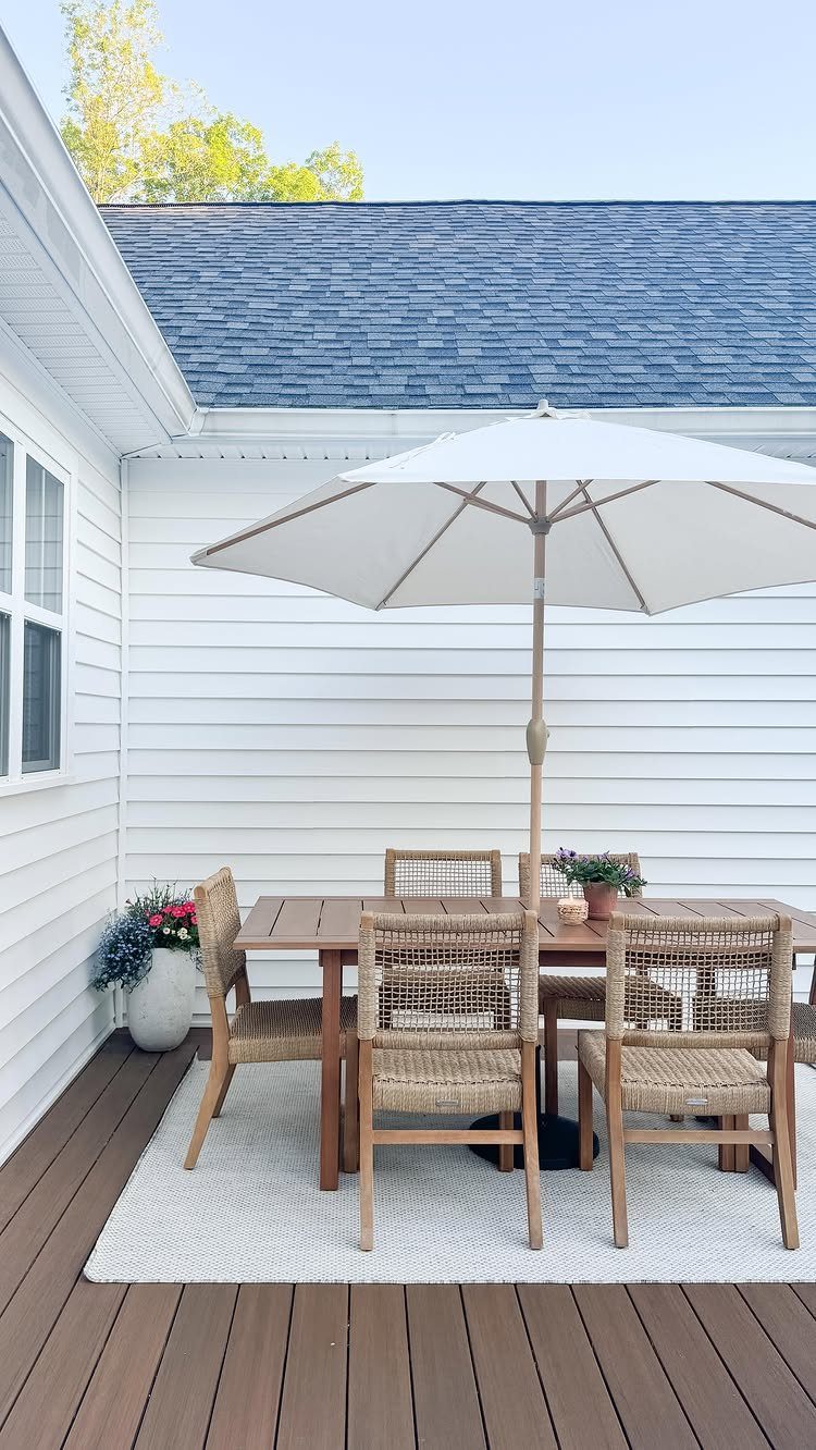 Rectangular wooden dining table with woven chairs and white umbrella on a deck.