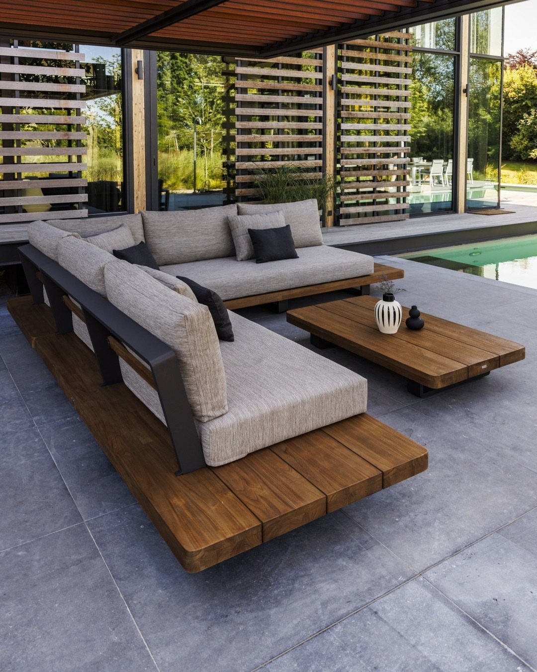 Grey sectional sofa on a wooden platform with a low coffee table by a pool.