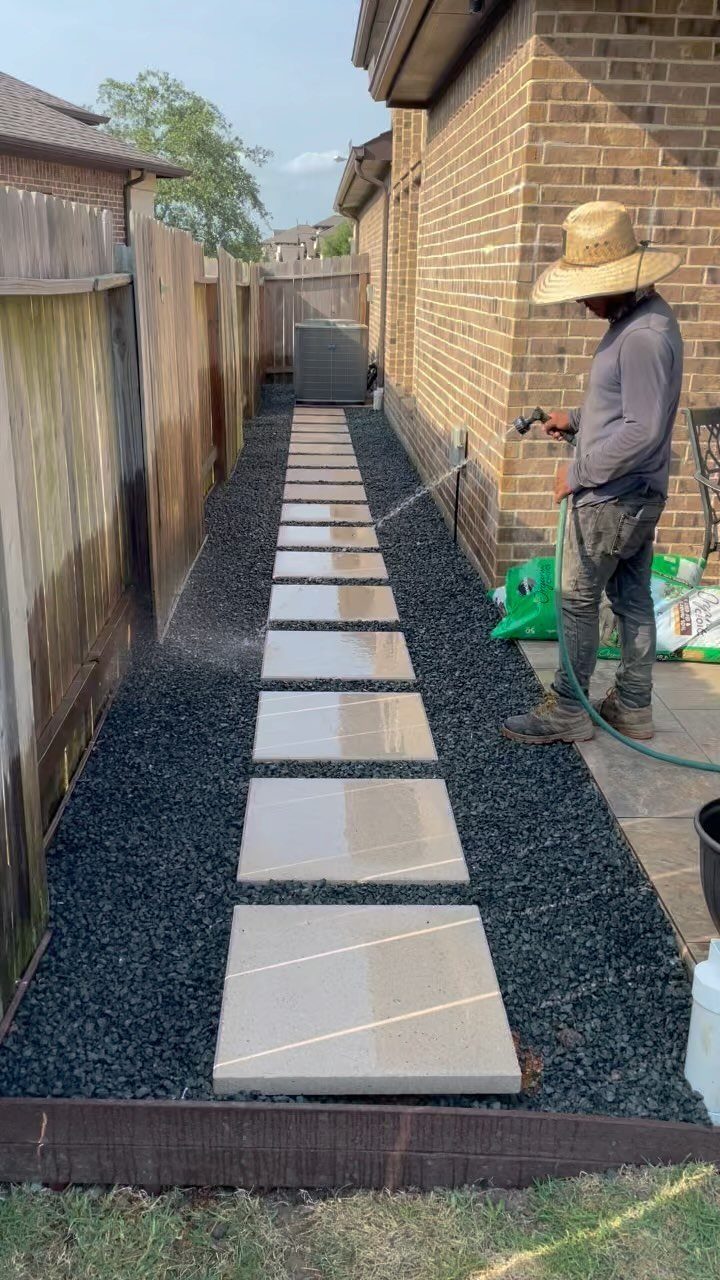 Square stone pavers set in dark gravel along a brick house and wooden fence.