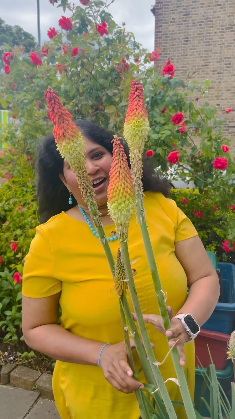 Woman in yellow dress holding tall Red hot poker plants with orange flower spikes.