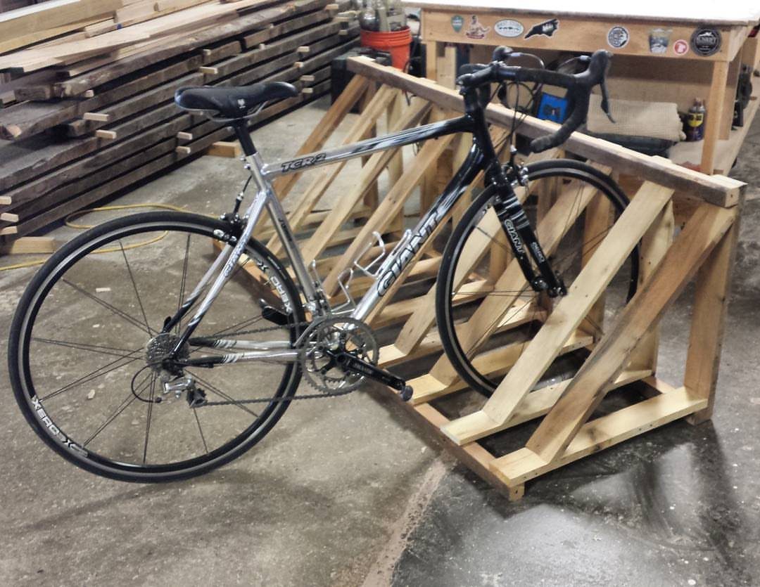 Silver road bike parked in a handmade wooden pallet bicycle rack in a workshop.