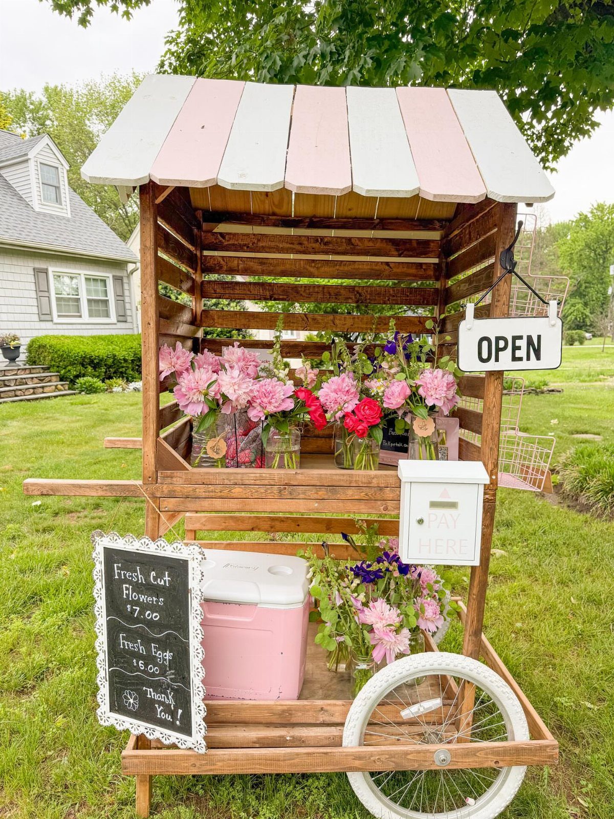 Rustic pallet wood garden cart with pink striped roof and fresh flowers on grass