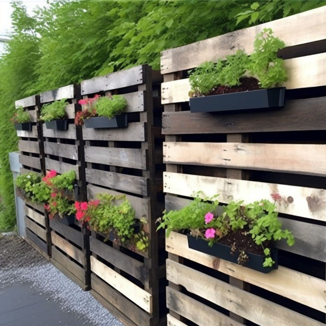Wooden pallet garden dividers with black planters holding pink and green flowers.