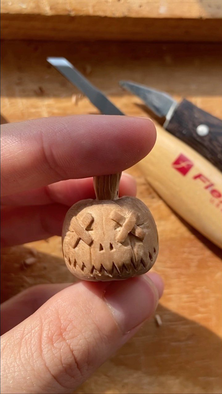 Small hand-carved wooden jack-o'-lantern pumpkin held between two fingers on a workbench.
