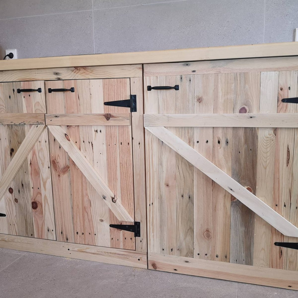 Rustic pallet wood kitchen cabinets with black hardware and a natural wood countertop.