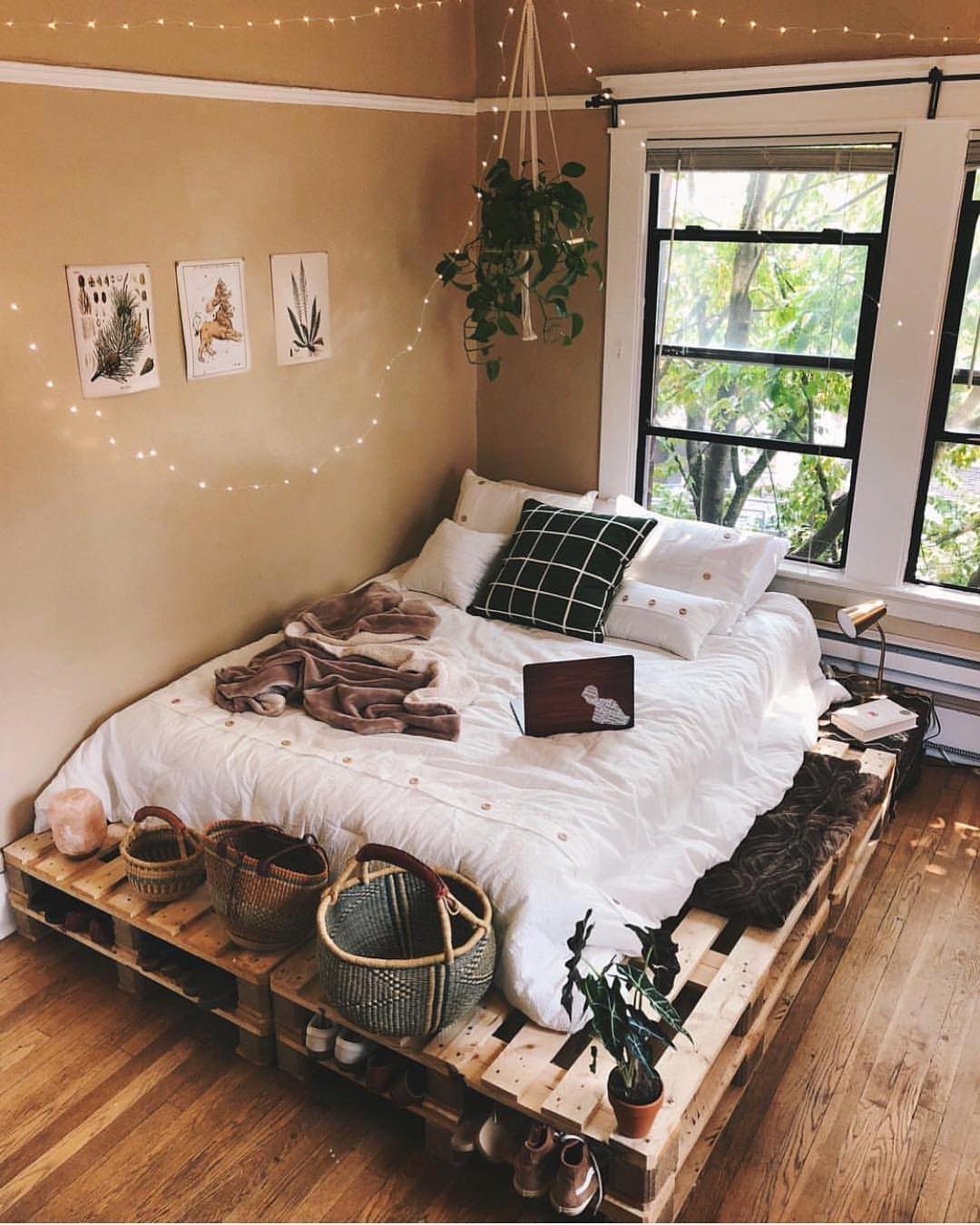 Bed with white linens on a light wood pallet frame in a cozy room.