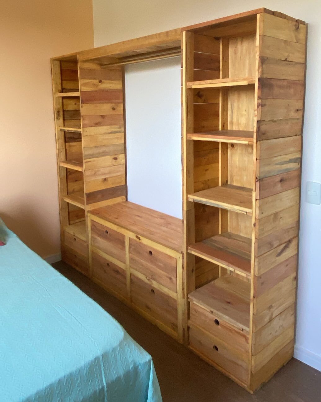 Wooden pallet shelving unit with side bookcases and a central dresser in a bedroom.