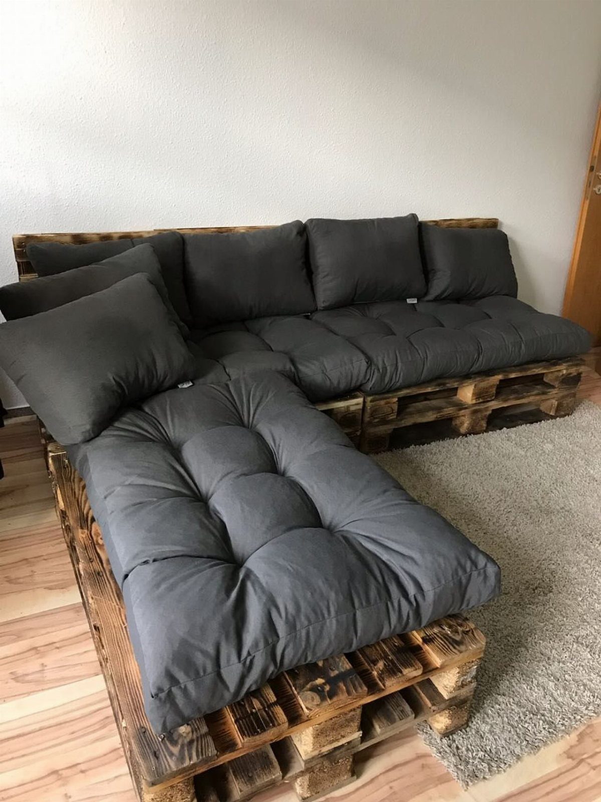 Sectional pallet couch with dark grey cushions on a light wood floor.