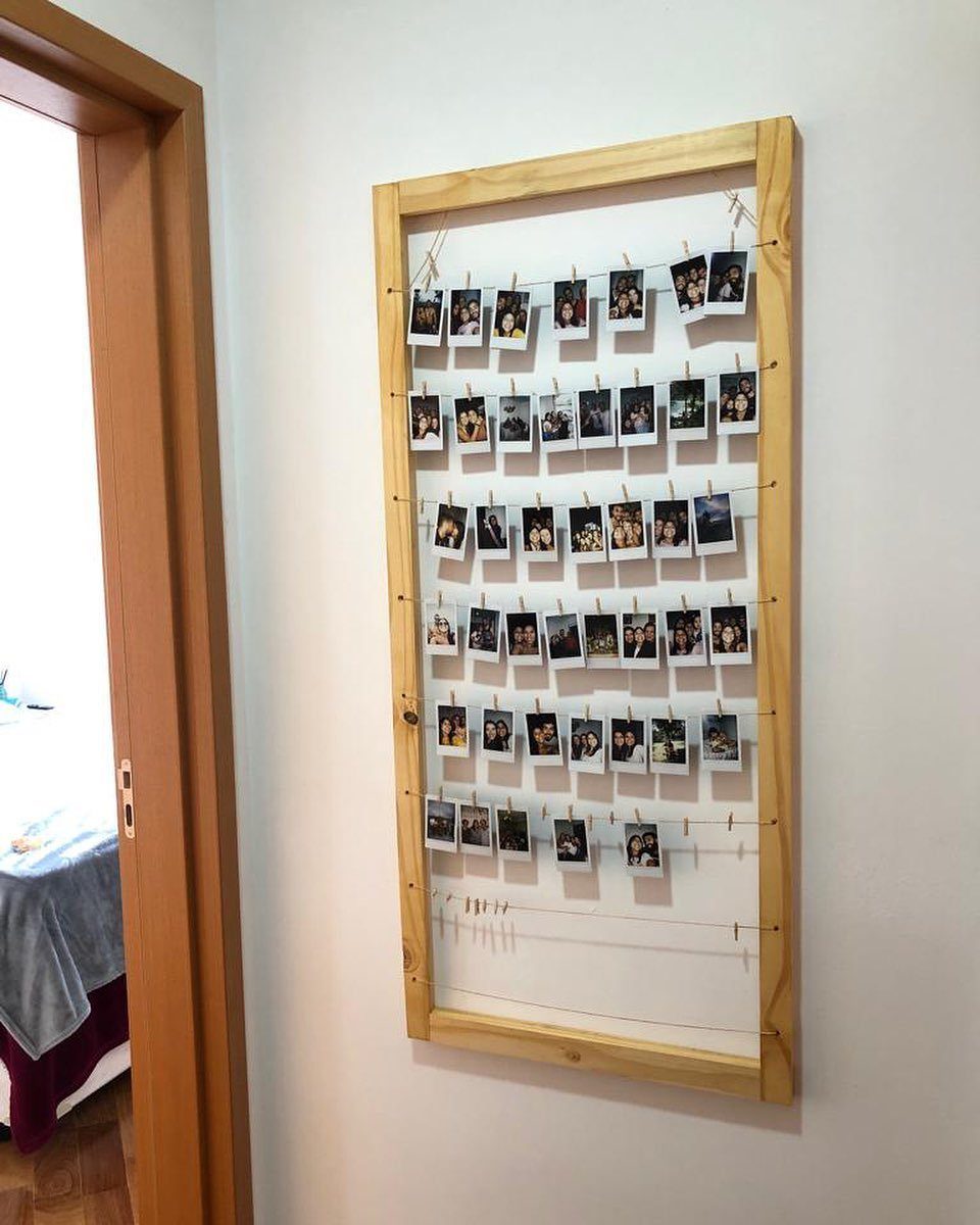 Wooden pallet frame holding multiple small photos clipped to strings on a wall.