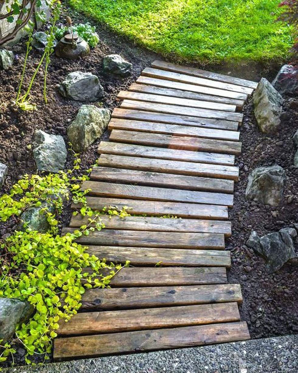 Wooden pallet slat walkway crossing through dark soil and garden rocks.