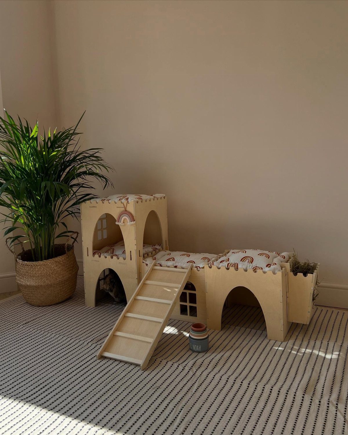 Wooden multi-level bunny house with a ramp and cushions on a striped rug.