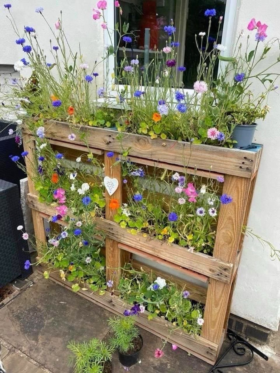 Vertical pallet planter filled with colorful wildflowers standing on a stone patio.