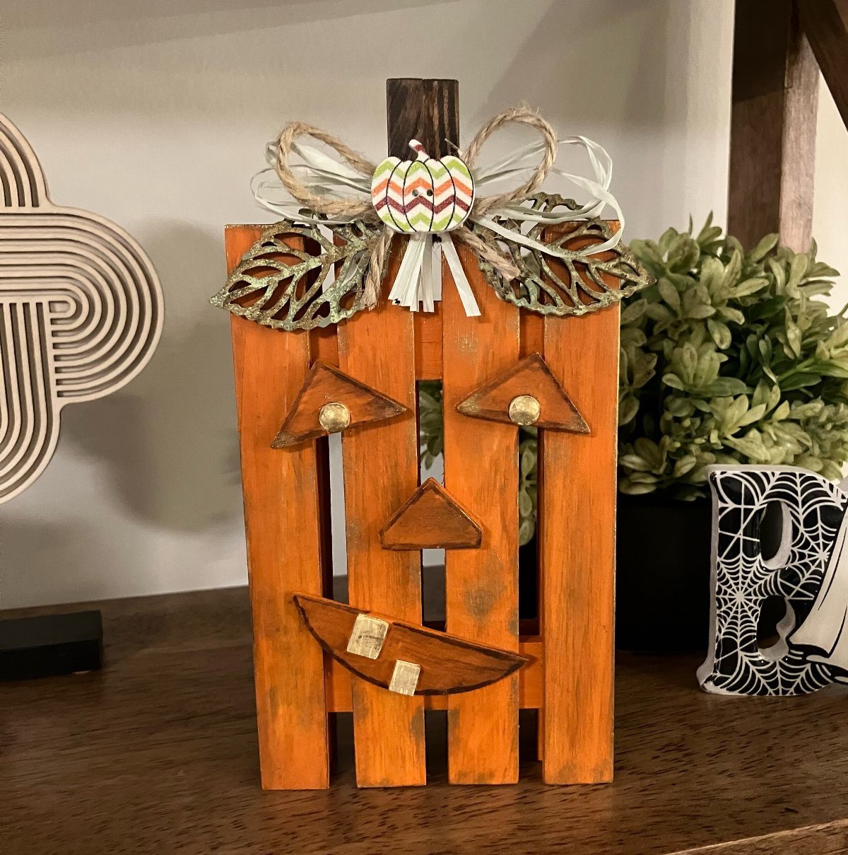 Rustic orange wooden pallet pumpkin decoration with a carved jack-o'-lantern face and bow.